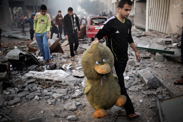 A Palestinian man carries a stuffed toy in a street littered with debris after an Israeli air raid on a nearby sporting centre in Gaza City, November 19, 2012 (Getty Images)